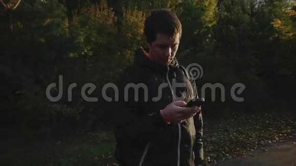 秋天公园穿黑色夹克的年轻人用智能手机上网视频的预览图