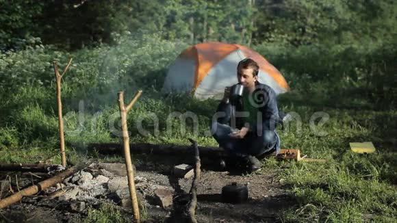 一个人喝茶在火灾附近点击电话背景是帐篷和美丽的森林视频的预览图