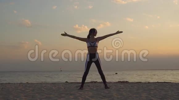 漂亮的年轻女子穿着运动服在户外练习瑜伽20岁的女孩黎明时分在海滩上做呼吸练习视频的预览图
