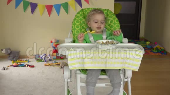 幼儿男孩坐在婴儿高喂养的椅子上用勺子吃土豆泥视频的预览图