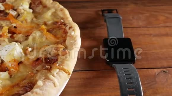 智能手表躺在木制桌子上旁边是自制的披萨里面有不同的奶酪和番茄移动摄像机视频的预览图