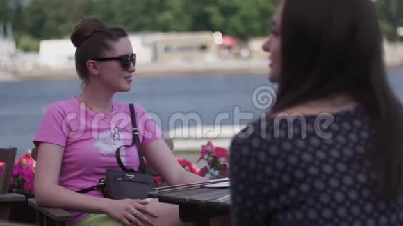 年轻女孩坐在海滨餐厅的露台上太阳镜朋友放松视频的预览图