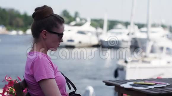 戴墨镜的年轻女孩坐在海滨餐厅的露台上休息视频的预览图