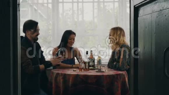 两个女孩和男人在桌子上说话在乡间别墅的露台上喝红酒视频的预览图