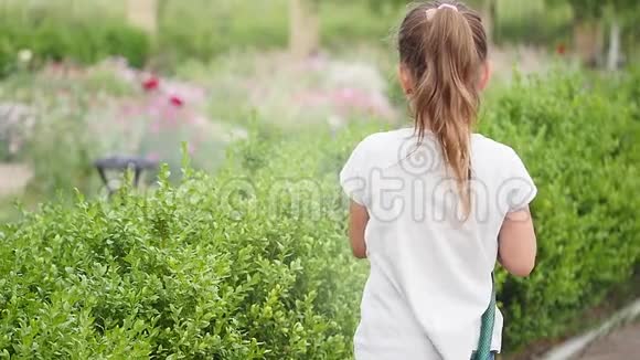 小女孩在花园里浇绿草可爱的小女孩拿着洒水器在草坪上喷洒视频的预览图