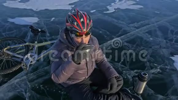 那个人正坐在冰上自行车的轮子上休息他喝热水瓶里的茶骑自行车的人穿着视频的预览图