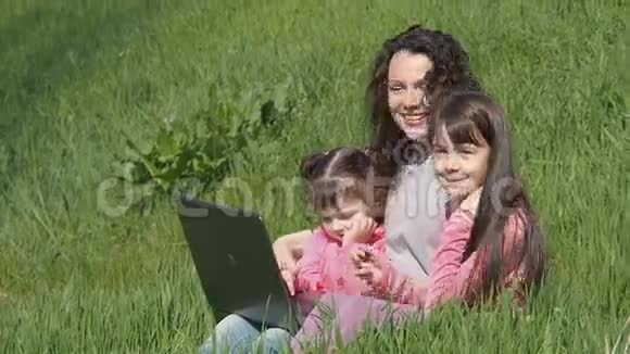 妈妈带着女儿在草地上拿着笔记本电脑阳光明媚的一天一家人在公园里视频的预览图
