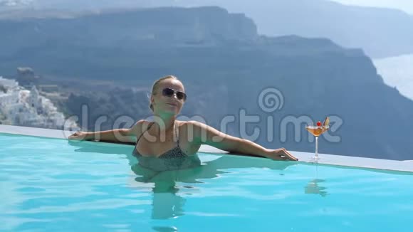 年轻女子在游泳池里放松欣赏桑托里尼的美景视频的预览图