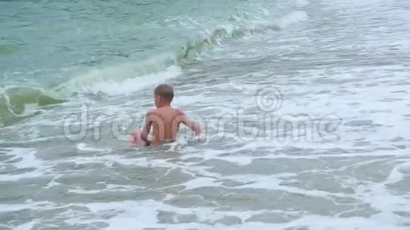孩子躺在沙滩上沐浴在大海的波涛中视频的预览图
