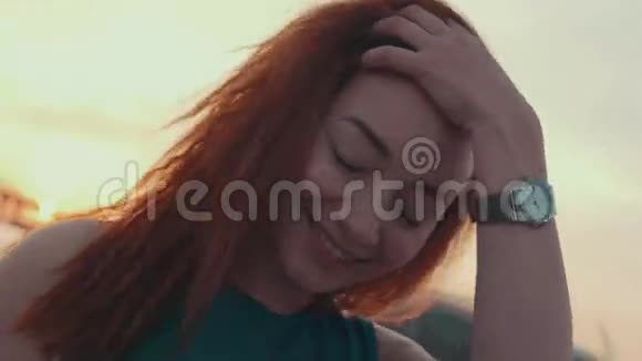 穿着绿松石衣服的年轻女孩在摩托艇上摸头发日落对着镜头微笑视频的预览图