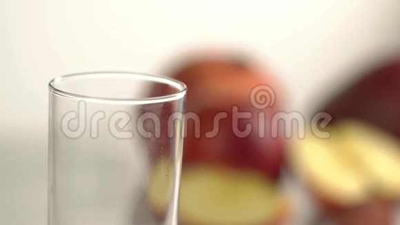 红色的饮料正倒入模糊水果背景下的空玻璃中特写镜头视频的预览图