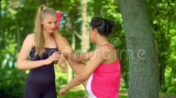 私人教练帮助女孩进行腿部伸展运动户外健身运动视频的预览图