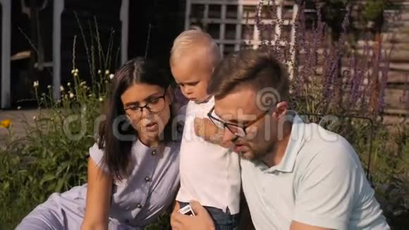 快乐的父母与儿子在院子里坐着时使用笔记本电脑视频的预览图