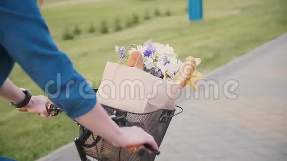 女孩的手放在自行车的车把上花和面包放在篮子里在城市里骑自行车慢节奏稳定的射击视频的预览图