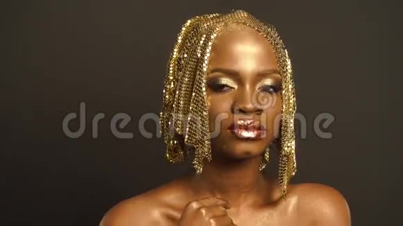 特写超现实肖像的光泽非洲裔美国妇女与明亮的金色化妆和头饰青铜体彩视频的预览图