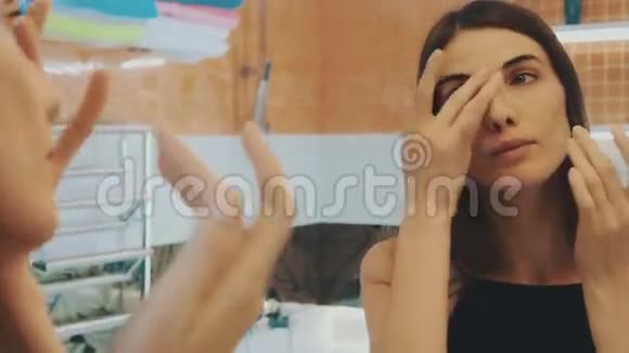 年轻的黑发女孩在浴室里照镜子摸脸摸脖子微笑视频的预览图