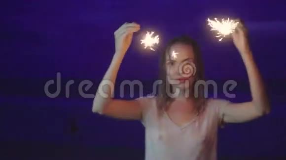 晚上在海滩上用闪闪发光的烟花为幸福的女人做特写视频的预览图