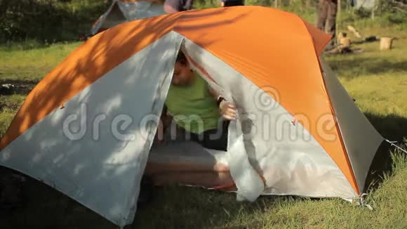 那人穿着鞋子走出营地的帐篷阳光明媚的一天在树林里在人们的背景下视频的预览图