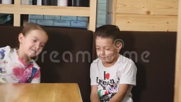 可爱的男孩和女孩坐在咖啡馆的桌子上玩视频的预览图