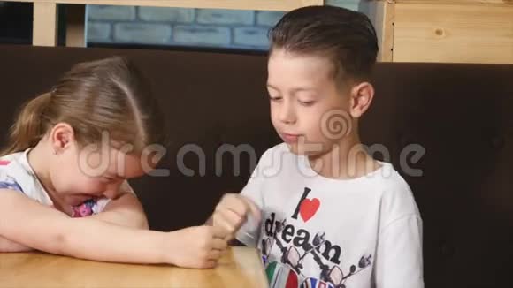 可爱的男孩和女孩坐在咖啡馆的桌子上玩视频的预览图