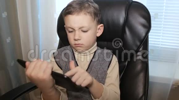 坐在皮椅上的男孩手里拿着平板电脑视频的预览图