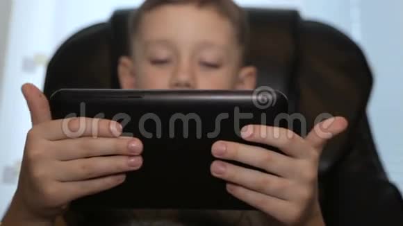 坐在皮椅上的男孩手里拿着平板电脑视频的预览图