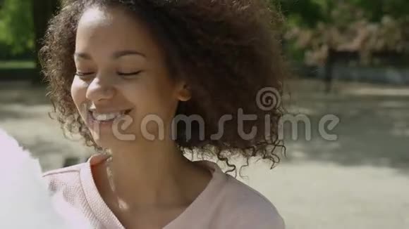 年轻的美国妇女在阳光明媚的公园吃棉花糖视频的预览图