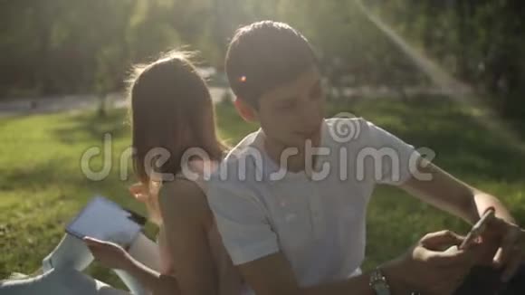 男孩和女孩背靠背坐在公园里的格子呢上特写镜头视频的预览图