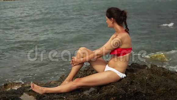 年轻漂亮的泳装女郎微笑着坐在海边的岩石上视频的预览图