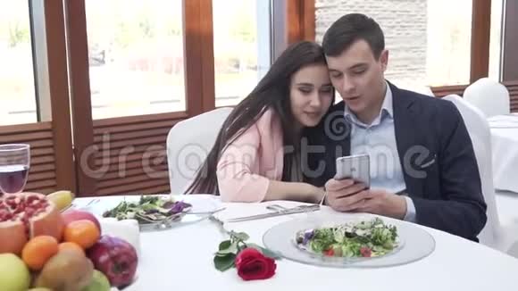 一对恋爱中的情侣在餐馆里浏览社交网络上的iPhone股票视频视频的预览图