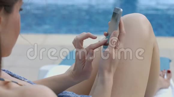 海滩上年轻女性在智能手机上输入信息的特写视频的预览图