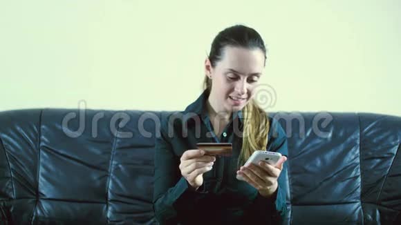 女士用信用卡和智能手机上网坐在背景模糊的沙发上视频的预览图