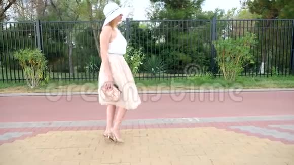 一个戴着帽子穿着白色风装的优雅女人漫步在海滨一般射击4k慢镜头视频的预览图
