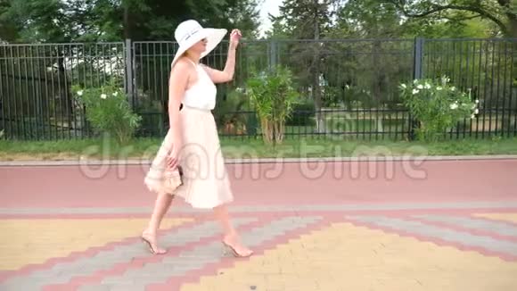 一个戴着帽子穿着白色风装的优雅女人漫步在海滨一般射击4k慢镜头视频的预览图