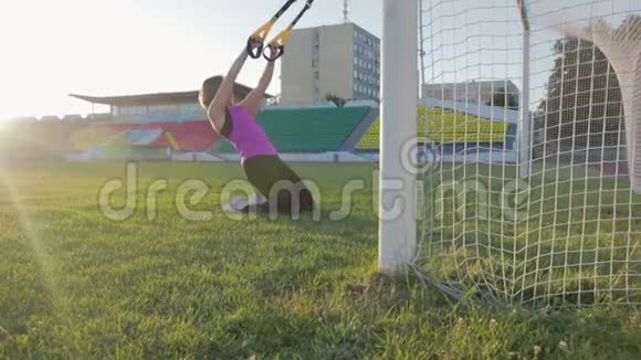 漂亮的健身女孩在体育场训练一个年轻的运动员在足球球门中在球场上绕圈子视频的预览图