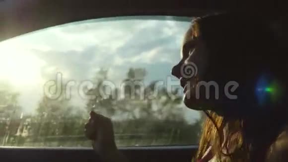 在阳光明媚的日子里坐在车上的年轻快乐的女士望着窗外欣赏着乡村的汽车唱着歌视频的预览图