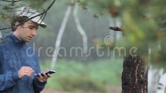 这个人在森林里的一棵树附近的电话上写短信清晨视频的预览图