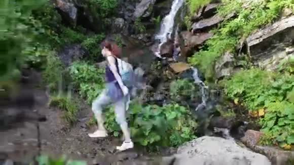 徒步旅行的女人背着背包走在山上的森林小径上背景是瀑布徒步旅行冒险视频的预览图