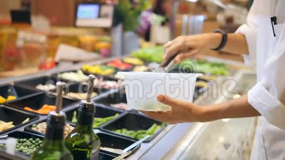 年轻的高加索女人在食品店的沙拉酒吧买有机蔬菜素食者带走食物健康饮食视频的预览图