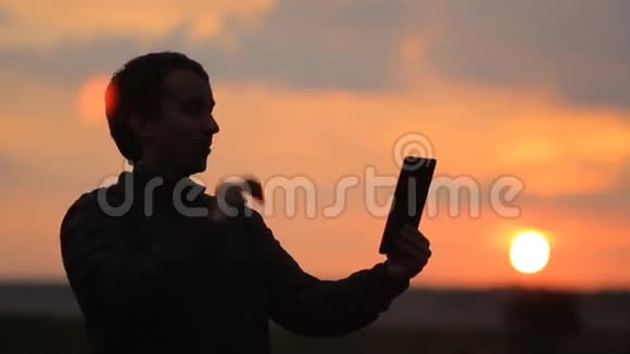 一个男人在平板电脑上打视频电话背景上美丽的日落视频的预览图