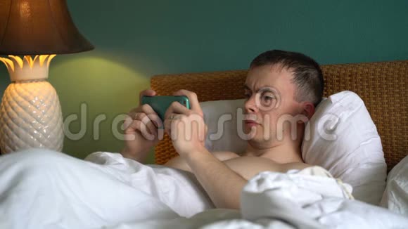 男人躺在床上正在使用智能手机上的应用程序视频的预览图