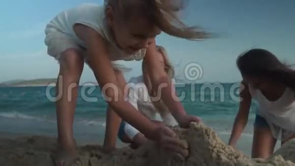 快乐的母亲和女儿在南海海滩上建造了一座沙堡慢动作股票录像视频的预览图
