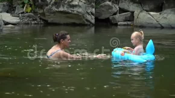 妈妈和女儿在河里一个年轻漂亮的女人正和她的小女儿一起在山河里洗澡他们是视频的预览图