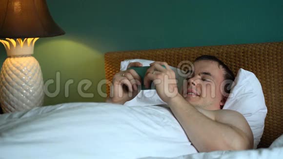 男人躺在床上正在使用智能手机上的应用程序视频的预览图