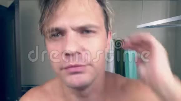 一个有趣的帅哥在浴室里用电动剃须刀刮胡子在镜子前唱歌4k视频的预览图