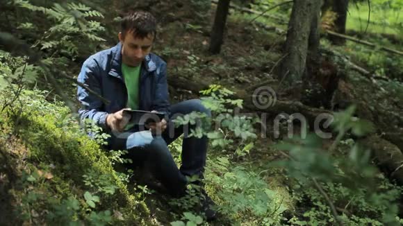 森林里的人在游戏中玩平板电脑它坐在绿色的小悬崖上视频的预览图