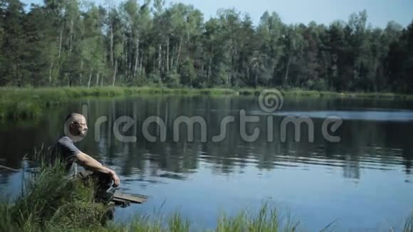 一个人坐在湖边的一个码头上欣赏着美景背景上美丽的蓝色湖泊和森林视频的预览图