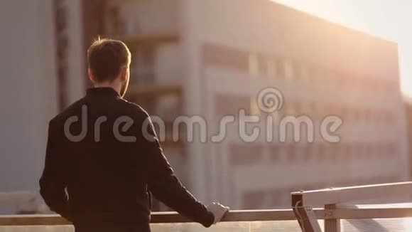 那个男人在他豪华公寓的阳台上站着日落背景视频的预览图