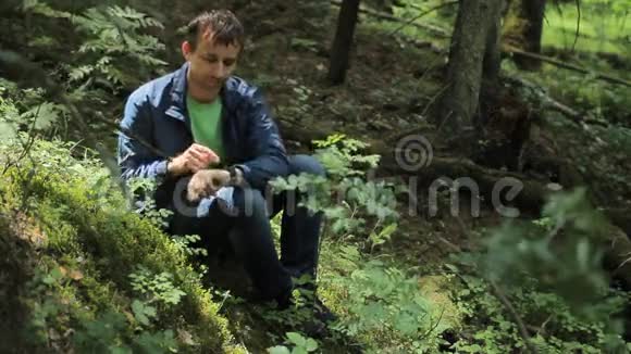 森林里的人摸着智能手表它坐在绿色的小悬崖上视频的预览图