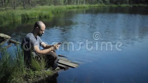 一个人坐在湖边的码头上在石碑上拍照背景上美丽的蓝色湖泊和森林视频的预览图